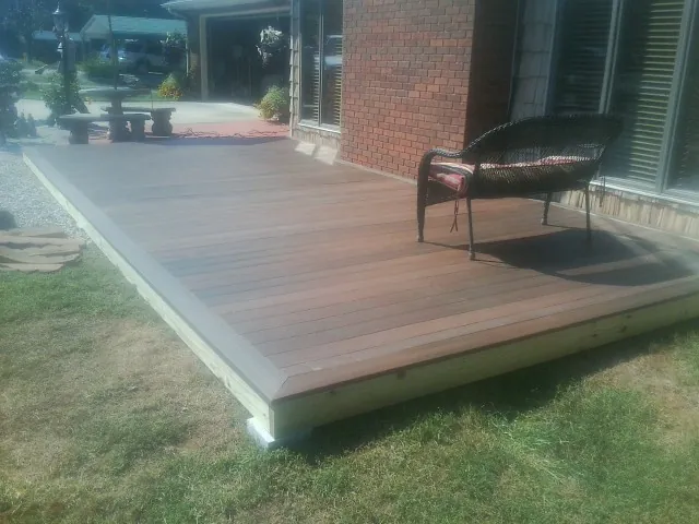 New wood deck and wicker chair beside a brick house in Randolph
